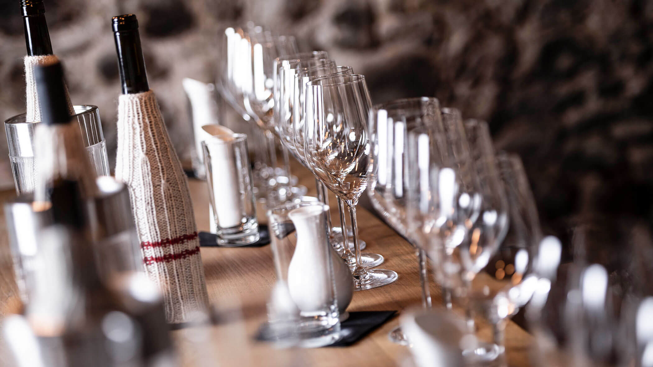 Close-up of empty wine glasses and bottles wrapped in covers on a wooden table, ready for a wine tasting.