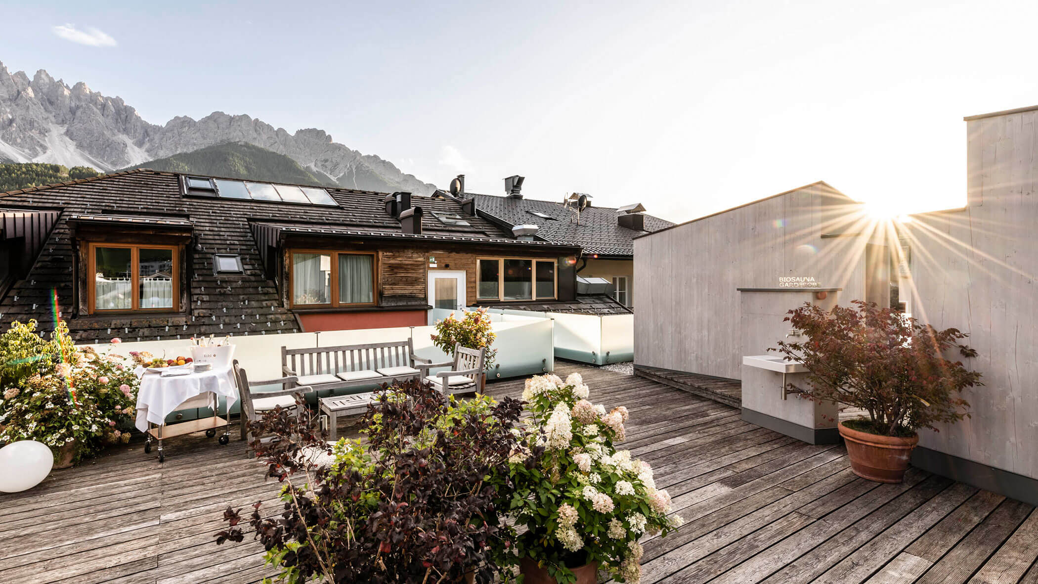 Terrazza sul tetto illuminata dal sole con piante in vaso, posti a sedere e vista sulle montagne sullo sfondo.