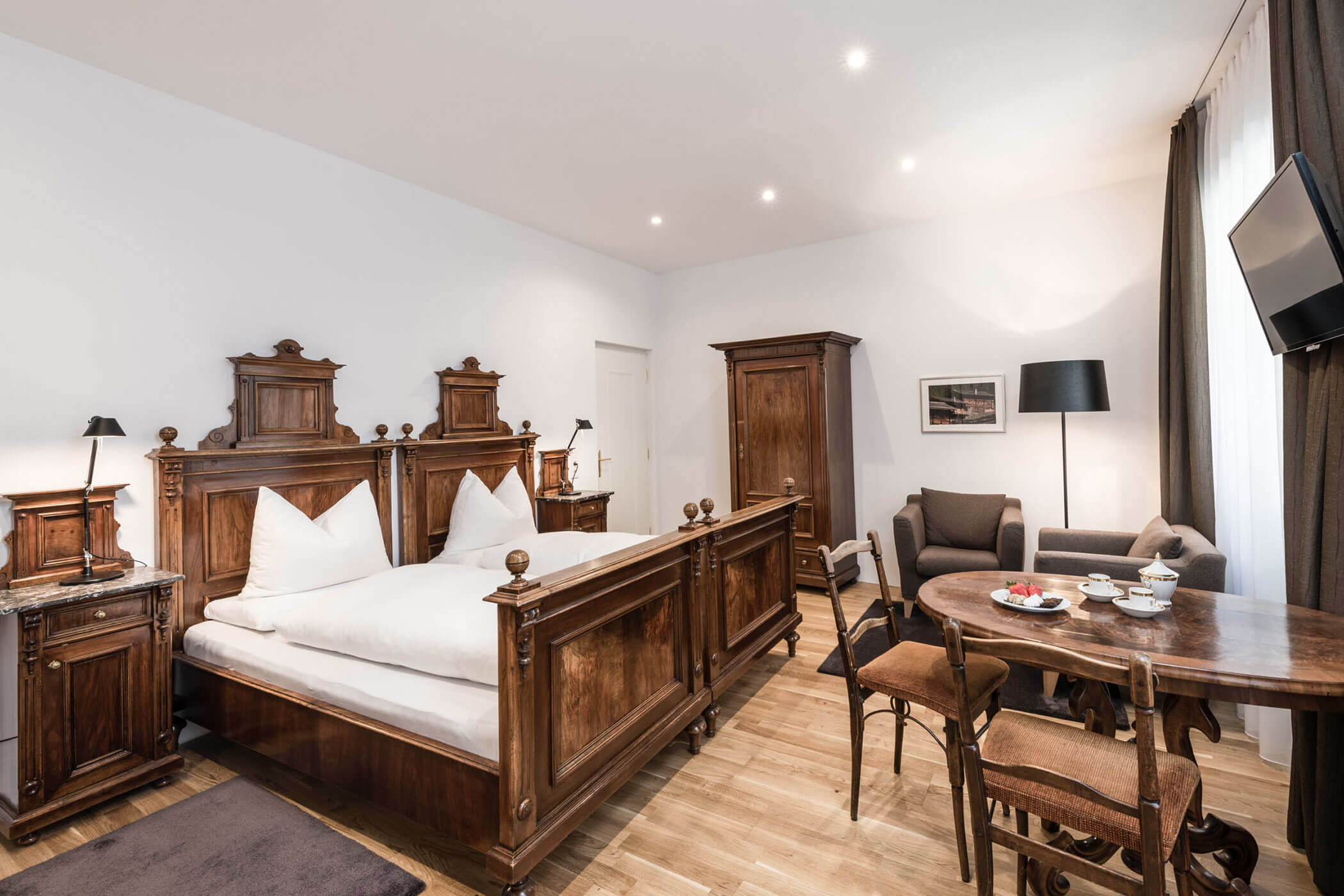 Spacious hotel room with antique wooden furniture, a double bed, seating area, and a table set for tea.