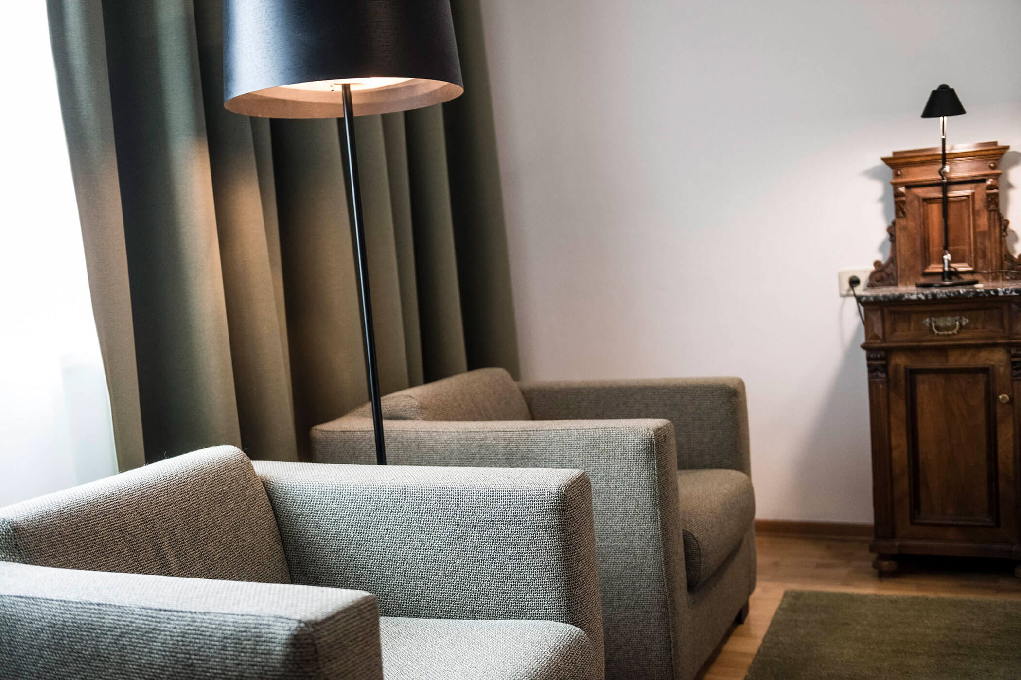 Two gray armchairs, a tall floor lamp, curtains, and a wooden cabinet in a cozy living room.