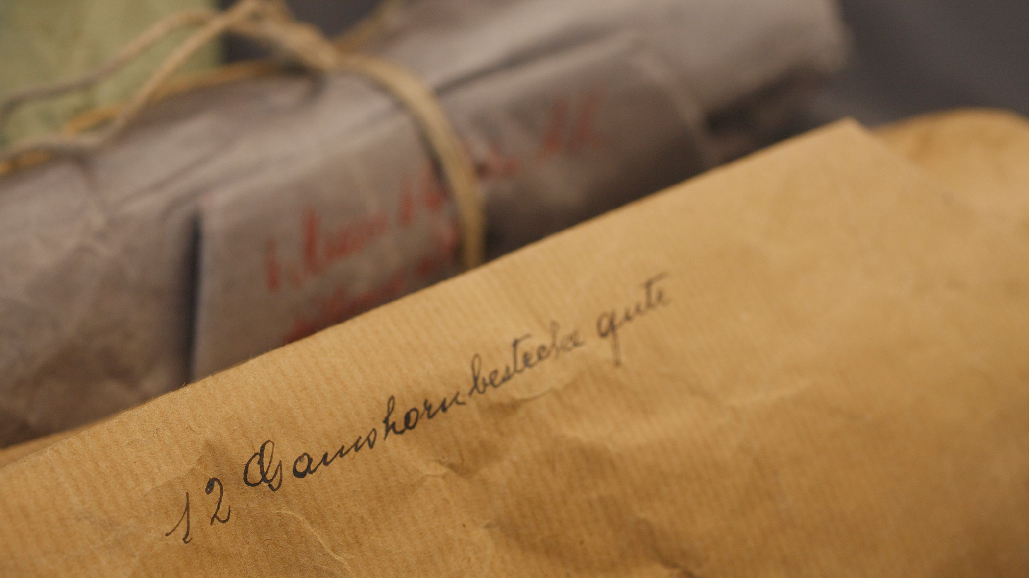 A close-up of a brown envelope with handwritten text and wrapped parcels tied with string in the background.