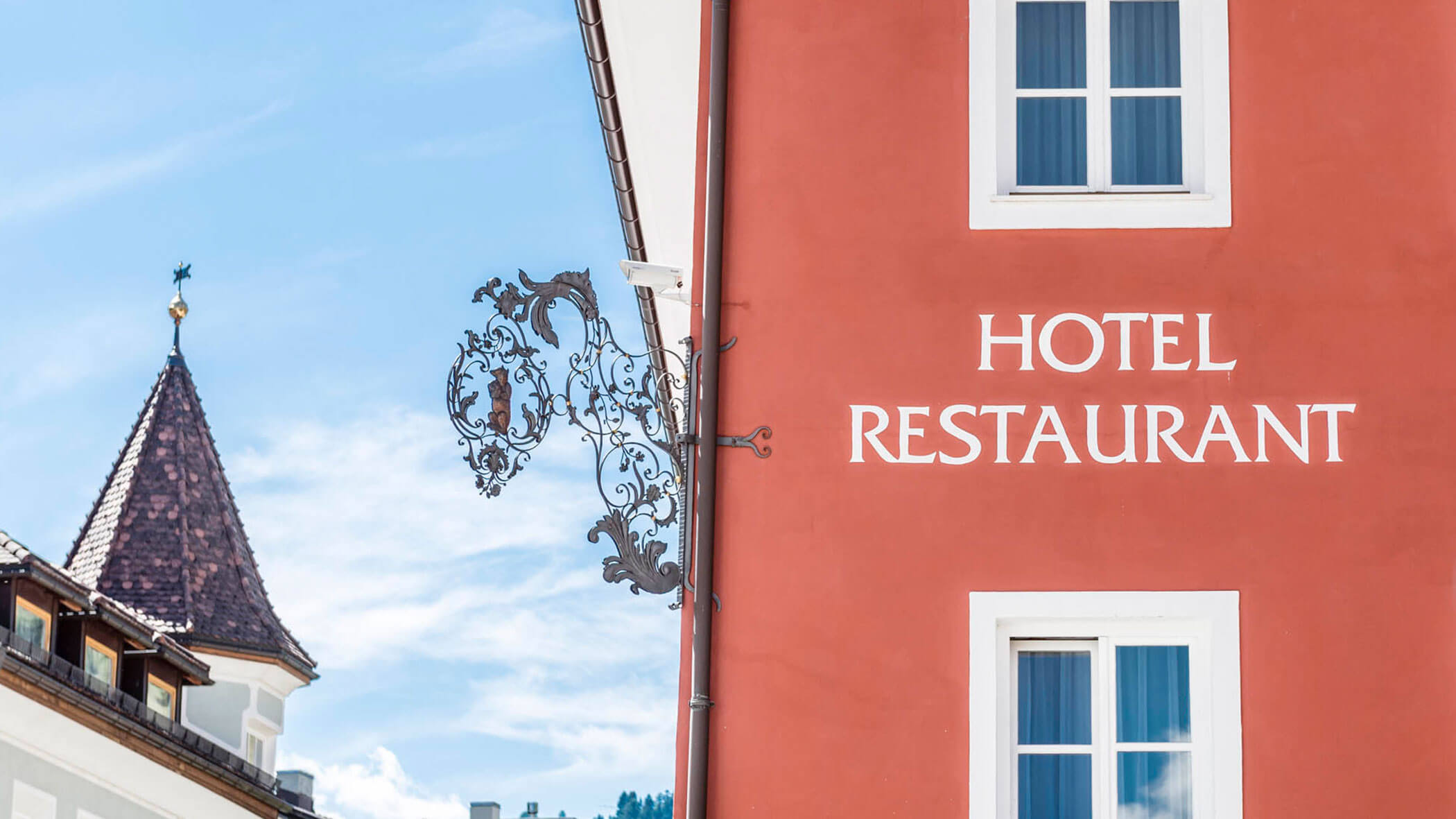 Edificio rosso con finestre bianche e insegna HOTEL RESTAURANT, decorazioni metalliche, cielo azzurro.