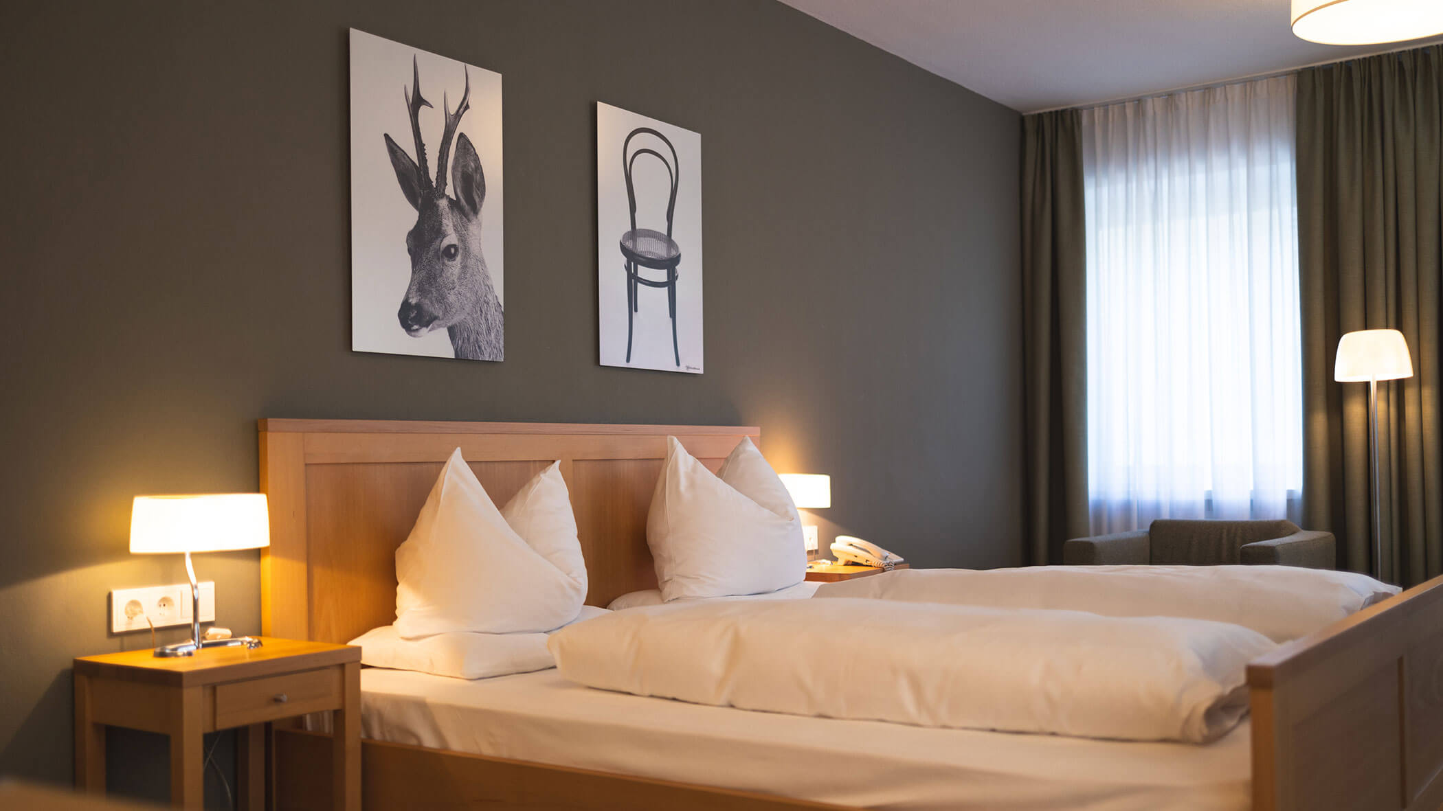 Cozy hotel room with double bed, two bedside lamps, and artwork of a deer and a chair above the headboard.