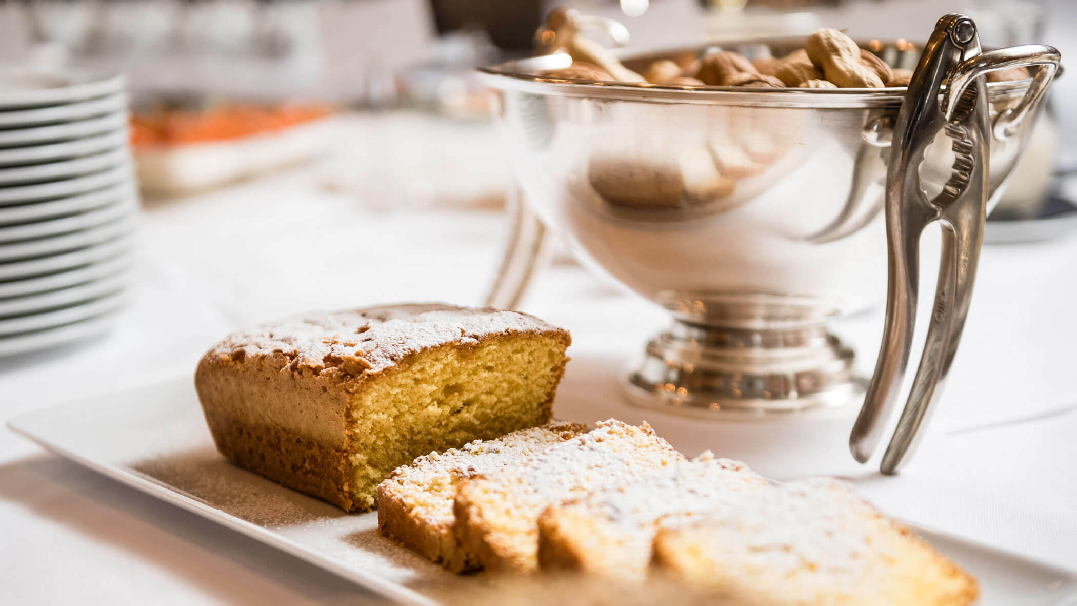 A loaf of pound cake with powdered sugar, partially sliced on a plate, next to a bowl of peanuts.