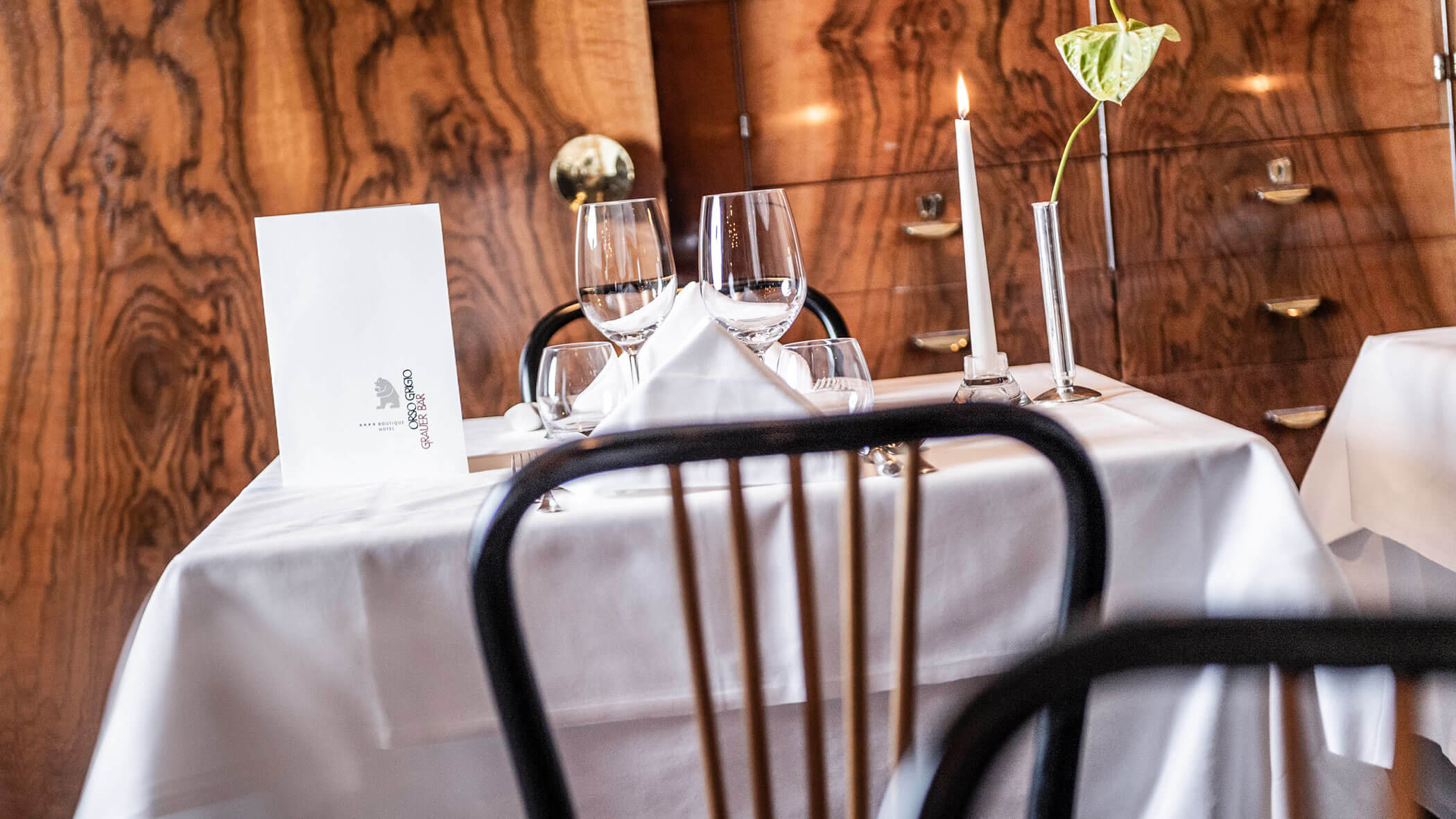 Elegant restaurant table set with glassware, a menu, a white napkin, and a lit candle on a white tablecloth.