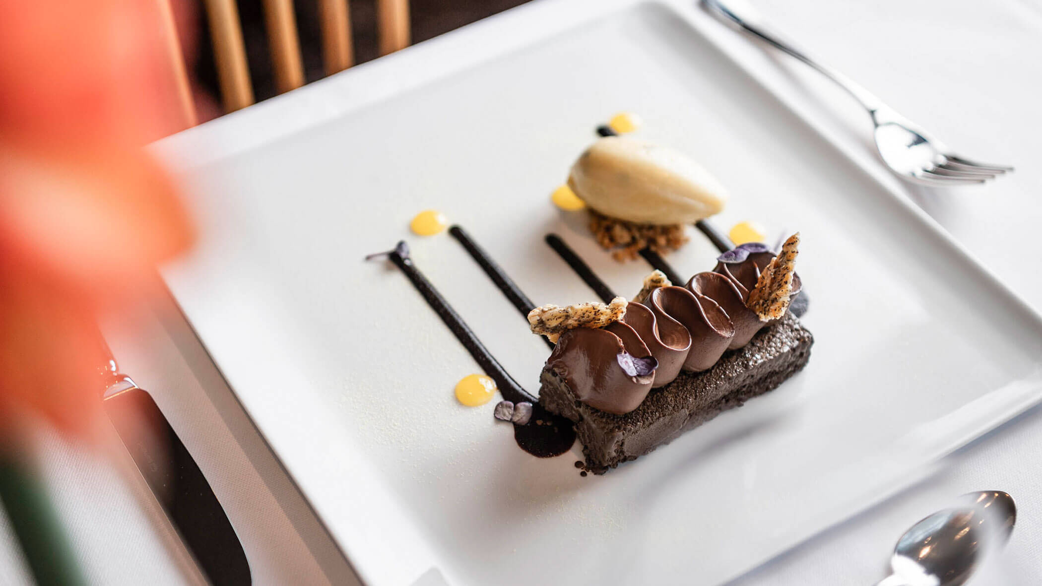 Elegant chocolate dessert with artistic sauce drizzles and a scoop of ice cream on a white plate.
