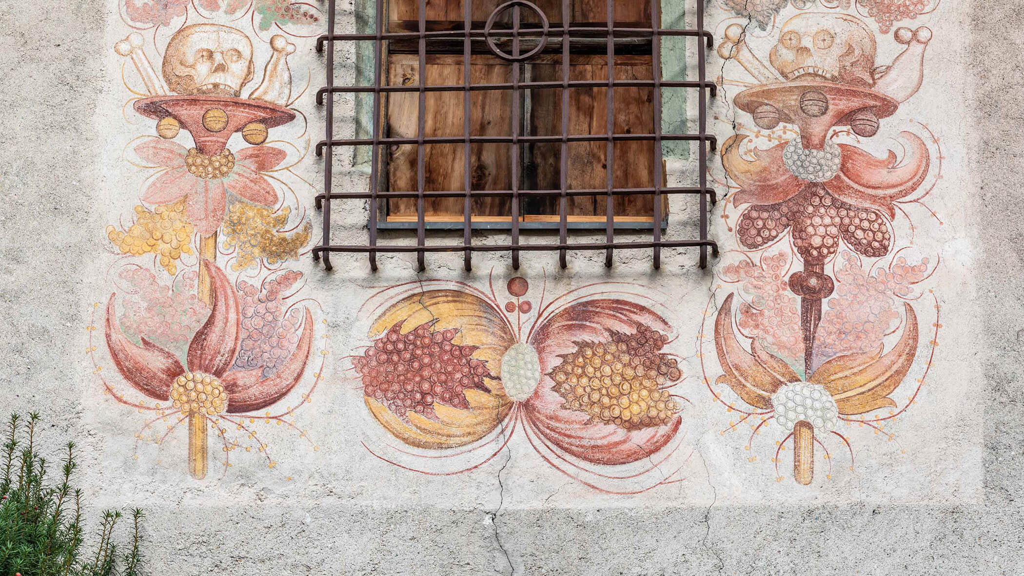 Mural of surreal flowers and skulls beneath a barred window on a textured wall.
