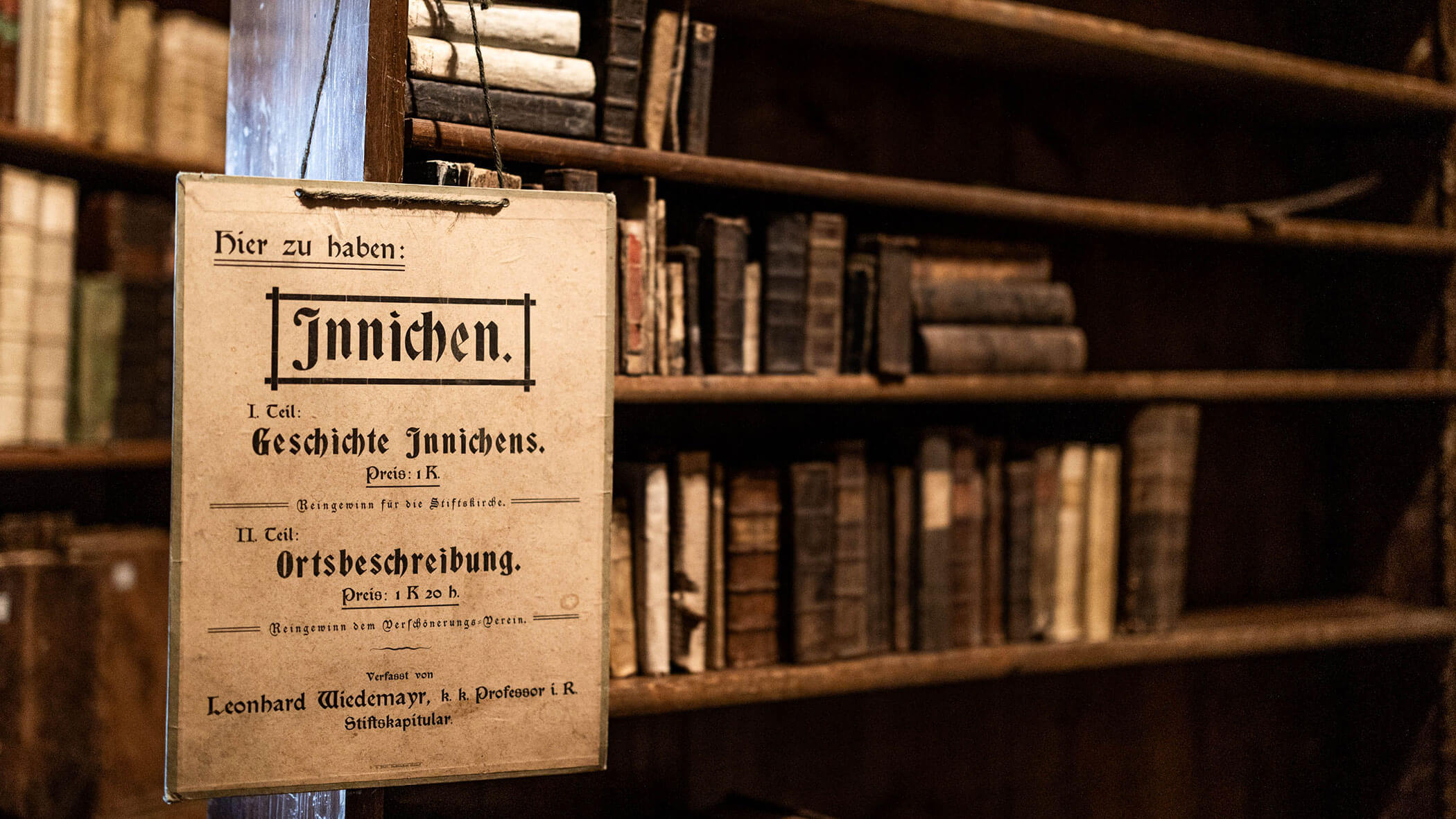 Un'insegna tedesca d'epoca è appesa davanti a vecchi libri su scaffali di legno in una biblioteca poco illuminata.
