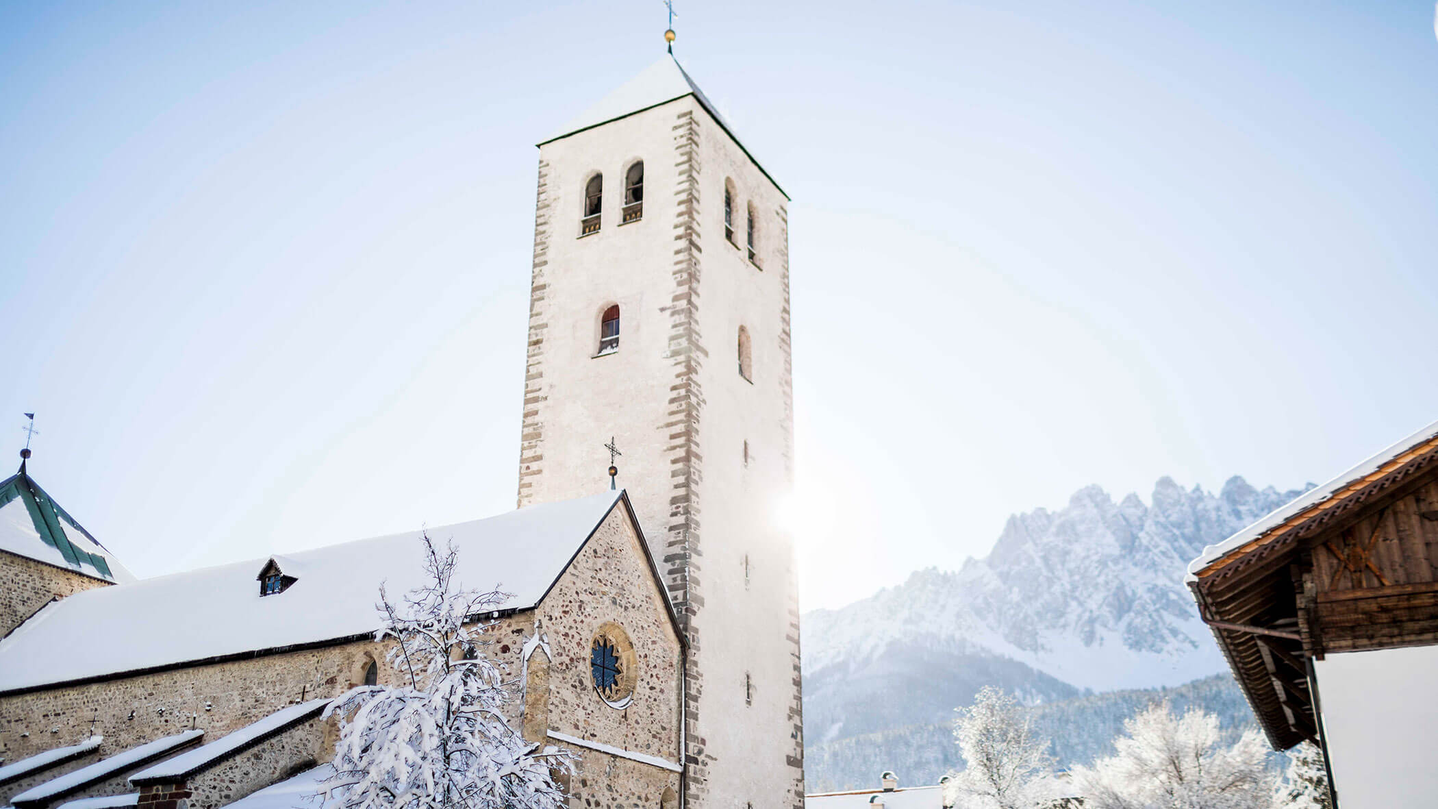 A stone church tower and snowy rooftops with mountains in the background on a clear winter day.