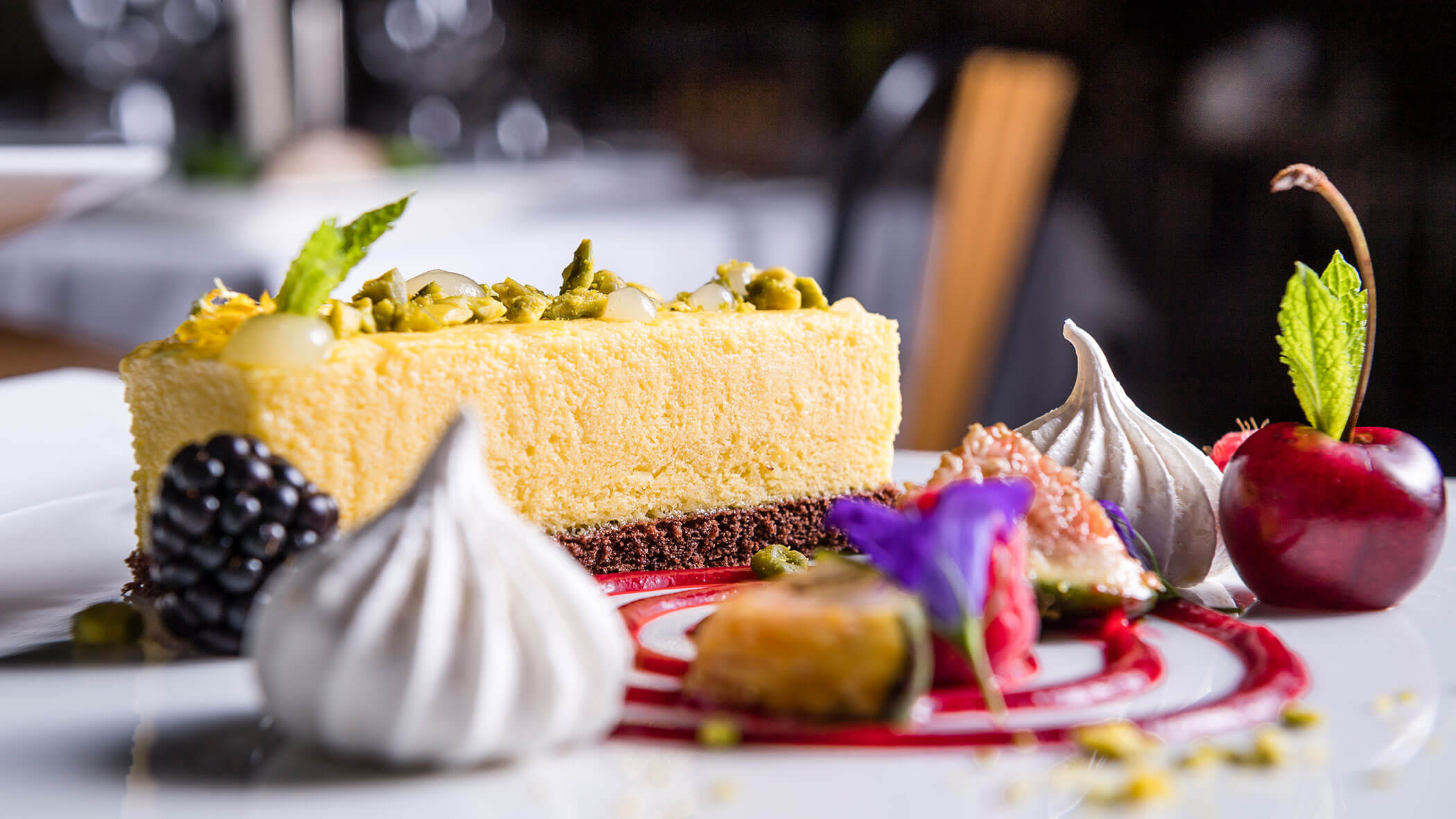A slice of cheesecake with berries, meringues, and mint garnish on a decorated dessert plate.