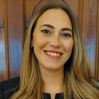 Smiling woman with long blonde hair in front of a wooden paneled wall.
