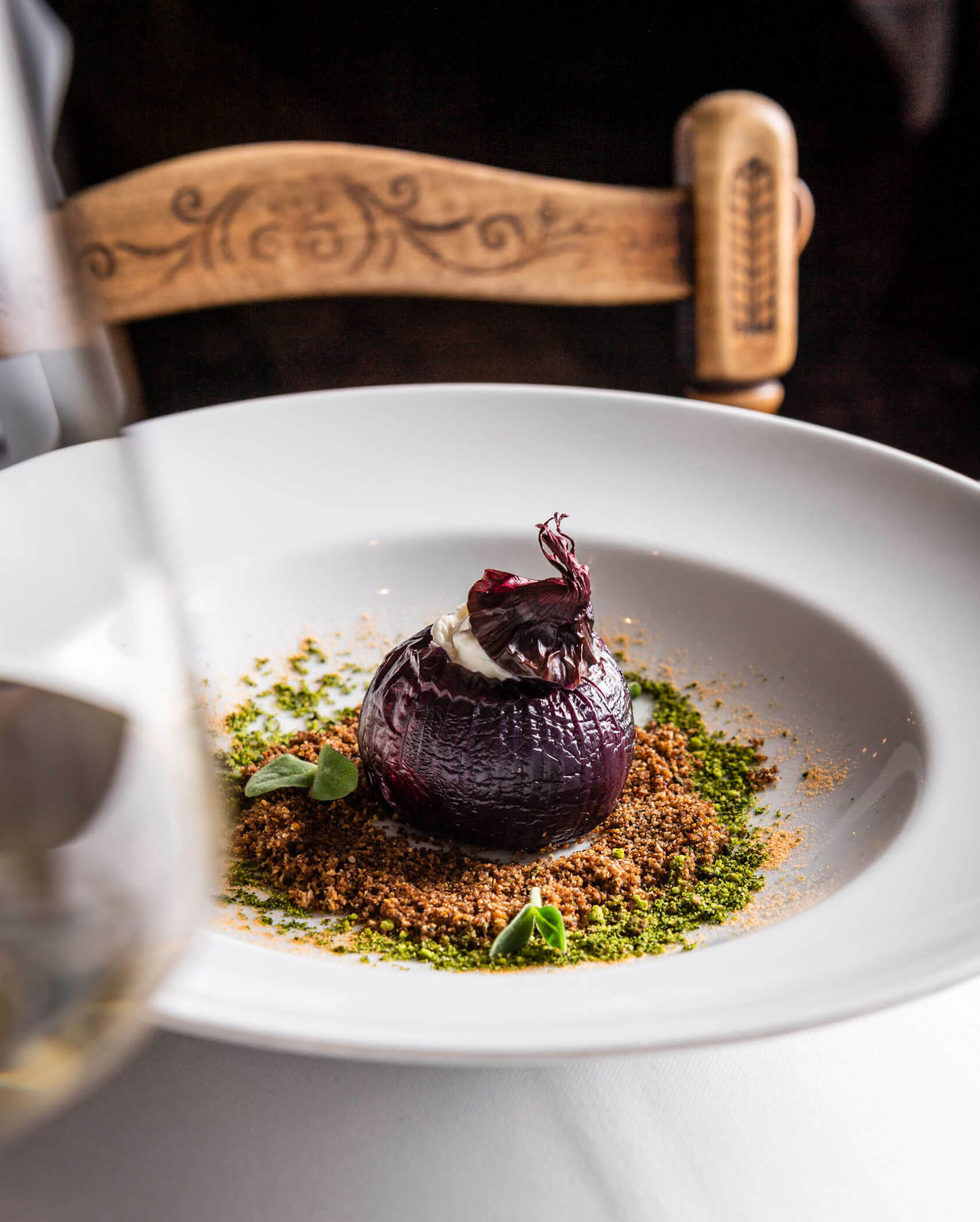 A gourmet dish featuring a stuffed roasted onion, garnished with herbs and crumbs on a white plate.