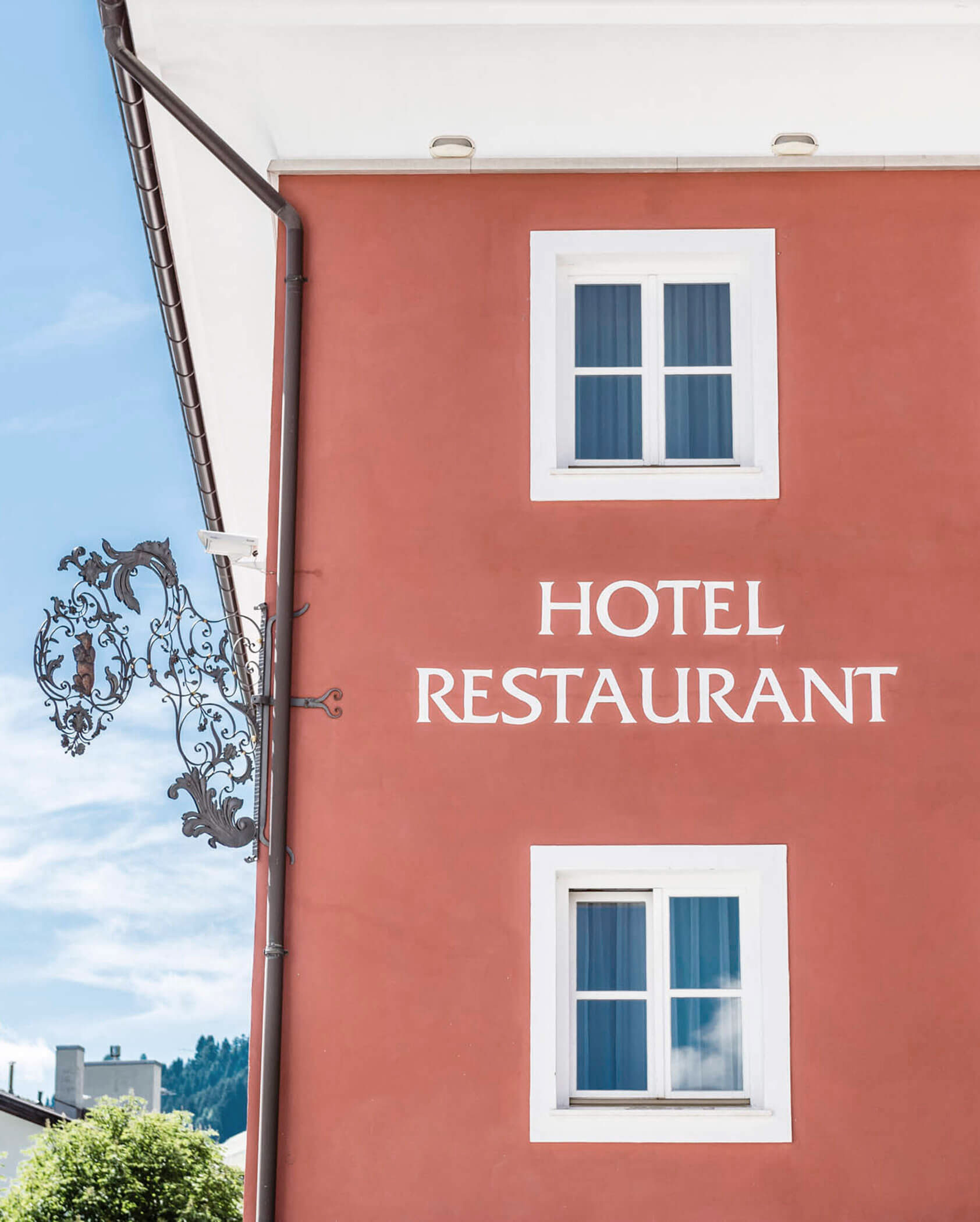 Red building with white-trimmed windows and ornate sign, labeled HOTEL RESTAURANT on the wall.