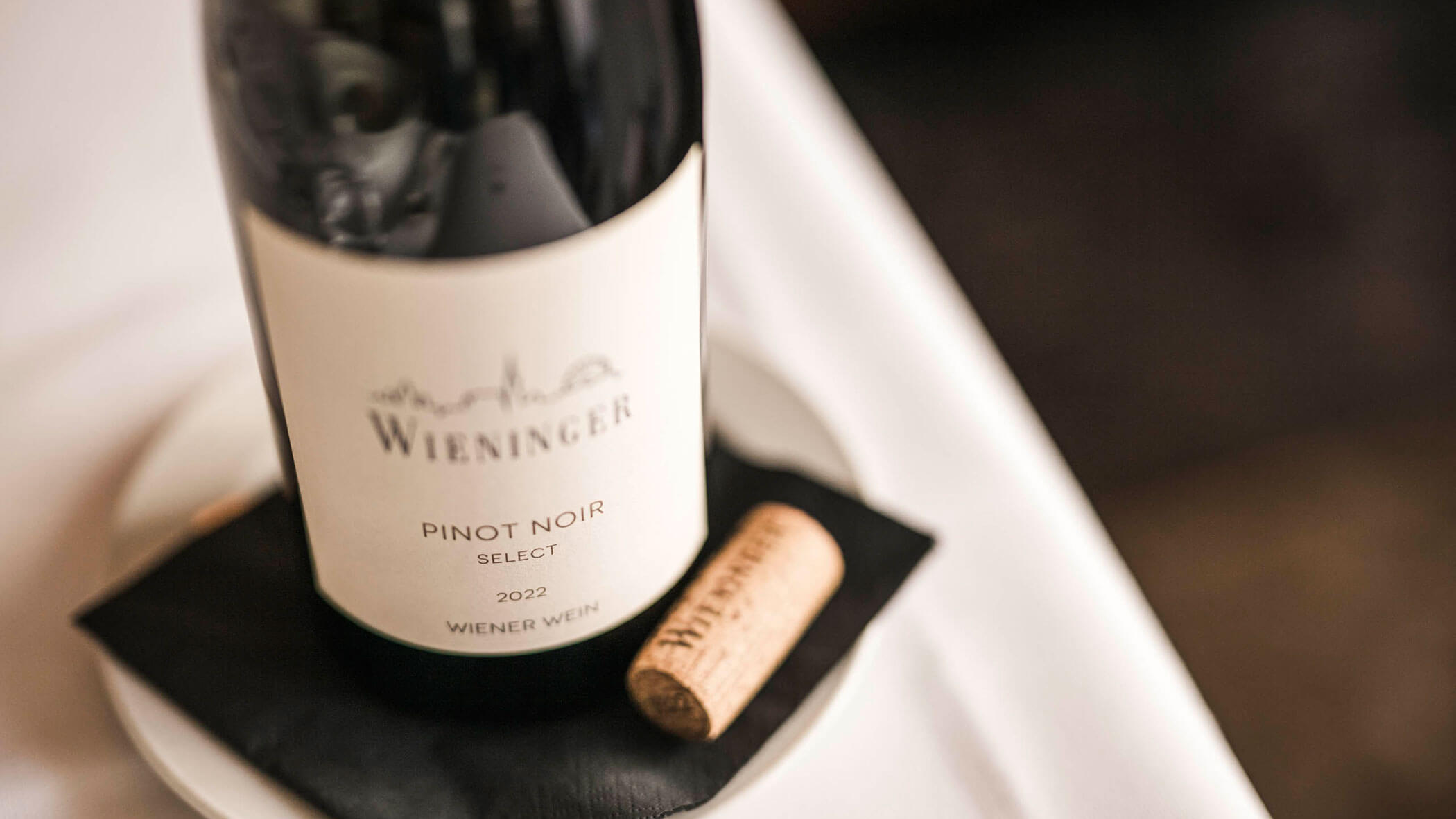 A bottle of Wieninger Pinot Noir wine and a cork on a small plate with a black napkin.