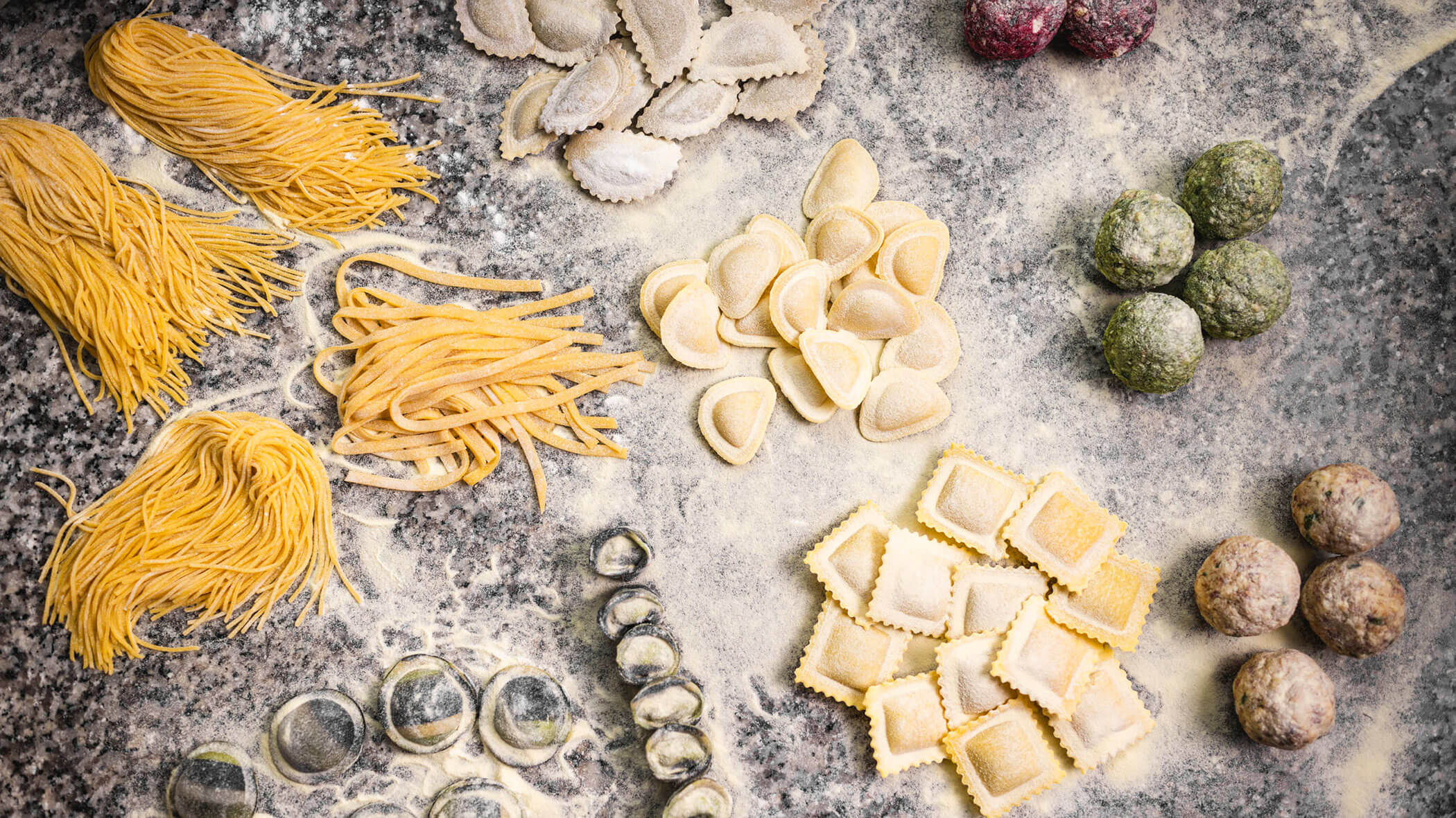 Assorted uncooked pasta and dumplings arranged on a floured surface, viewed from above.