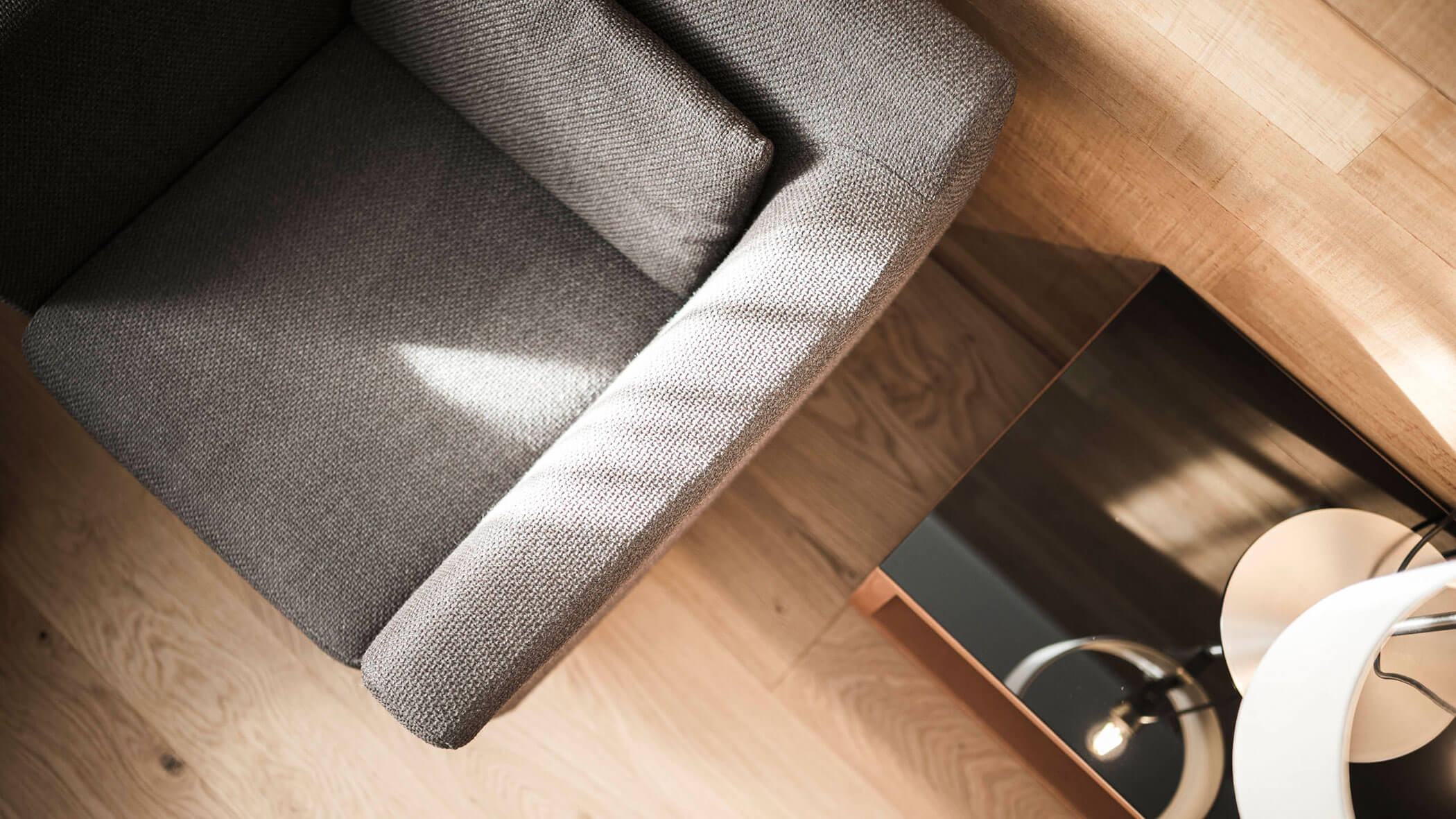 Top view of a gray armchair on a wooden floor next to a black side table and a white desk lamp.